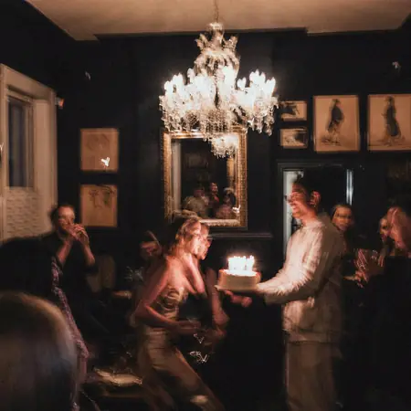 Um bolo de aniversário com velas acesas sendo levado para a mesa.